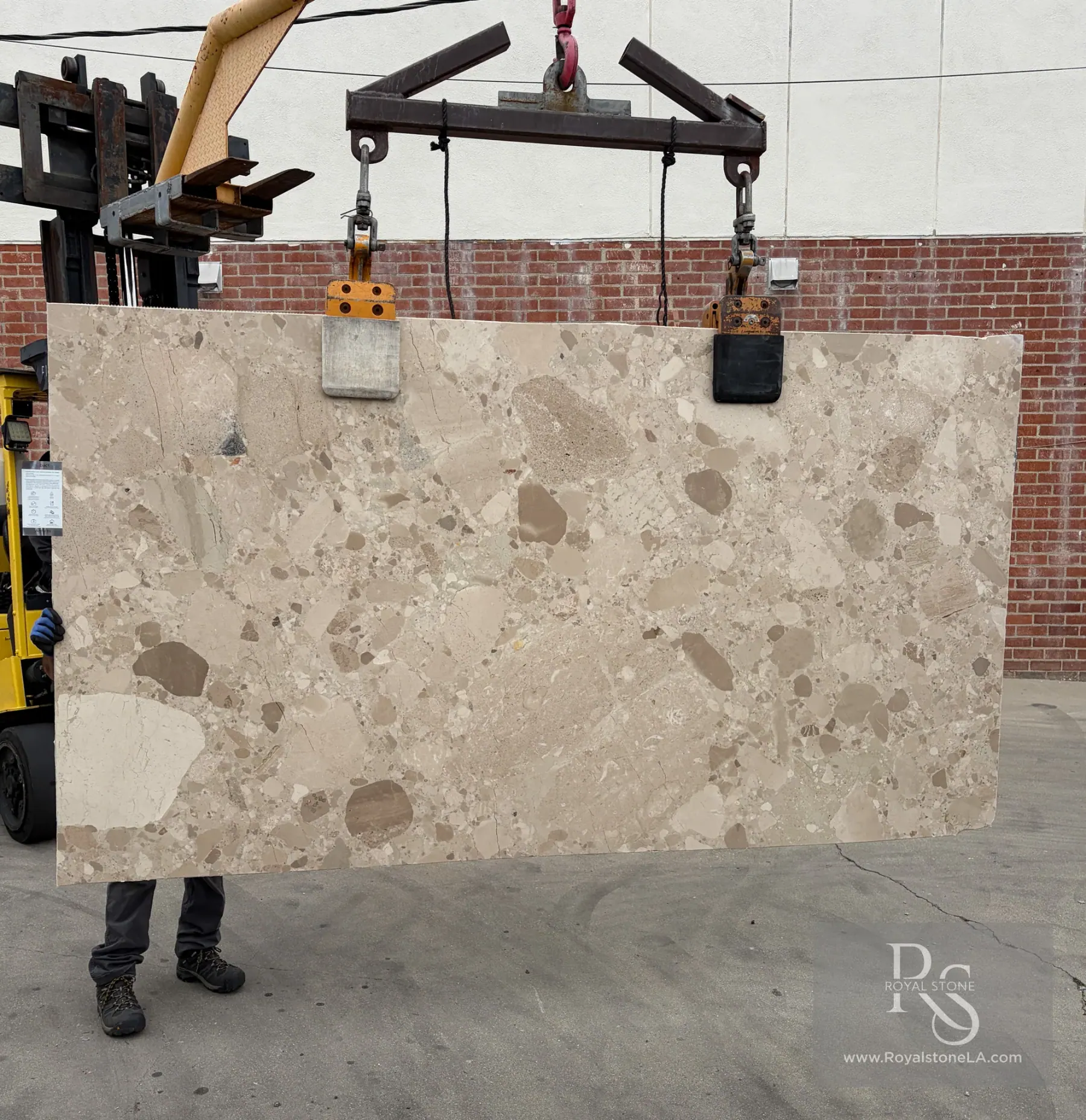 2cm Antolini Ceppo Beige Avorio EF299 marble slab, honed, 63 by 114 inches, ivory field broken by taupe and oatmeal clasts with a few darker grey fragments, lifted on a forklift against a brick wall at the Royal Stone yard in Los Angeles