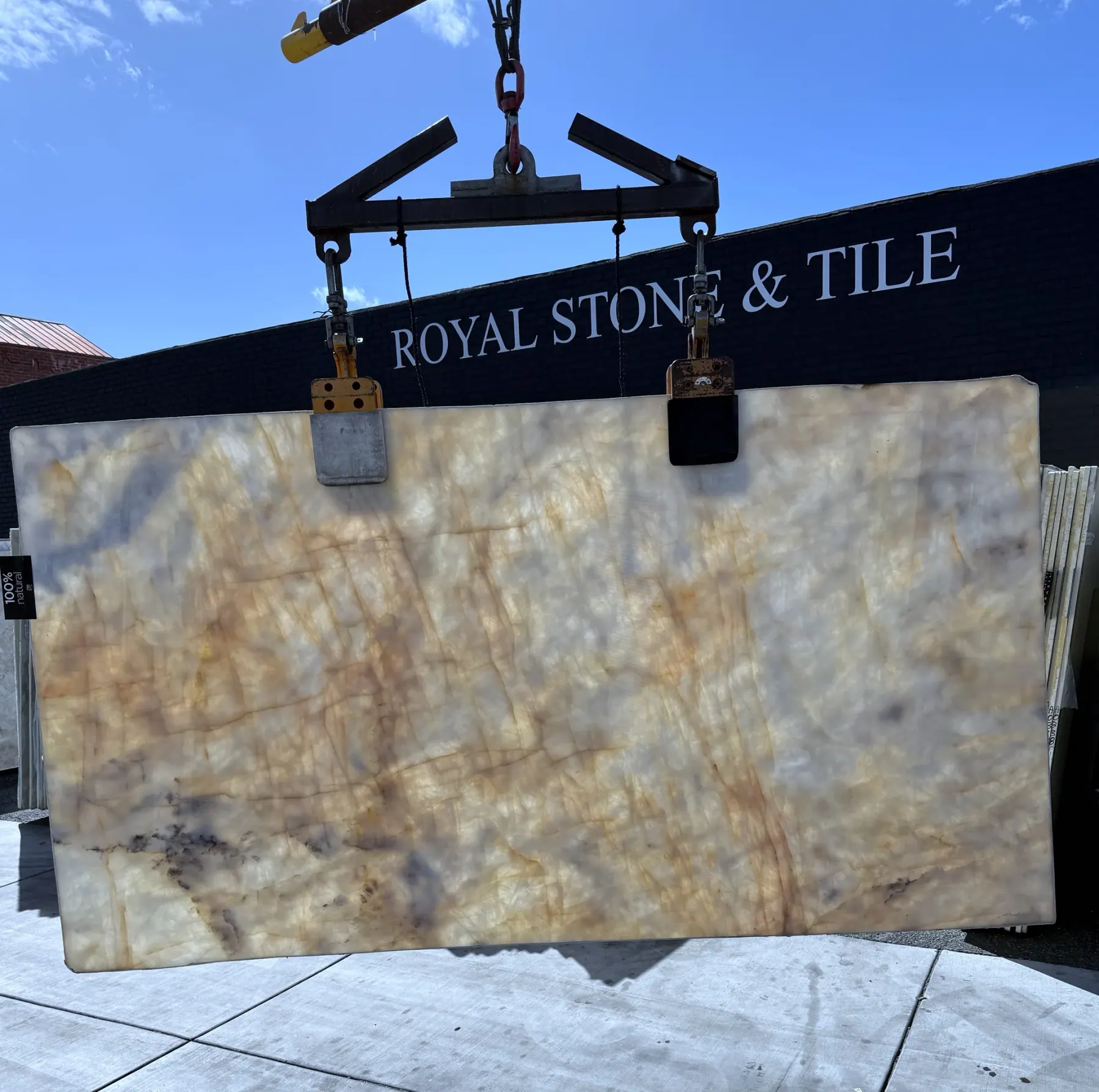 2cm Antolini Cristallo Brut Champagne AN568B polished quartzite slab backlit, the ivory field glowing gold and the honey veining lit up like cut amber against the Royal Stone wall