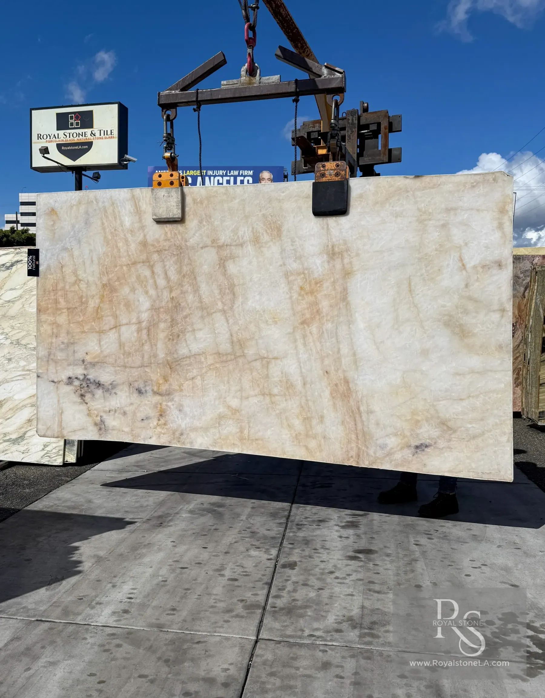2cm Antolini Cristallo Brut Champagne AN568B polished quartzite slab, 69 by 125 inches, ivory-champagne field with soft honey and caramel veining and a few charcoal inclusions, lifted by crane in front of the Royal Stone sign in Los Angeles