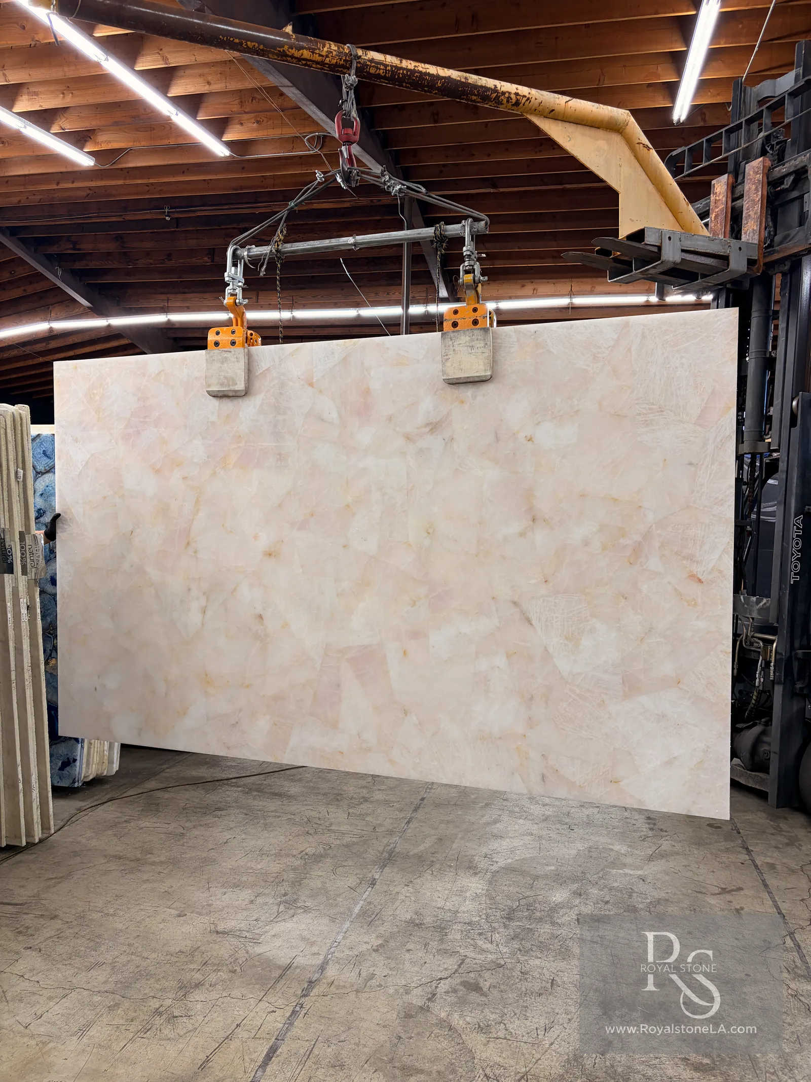 2cm Antolini Precious Stone Crystal Baby Rose slab, polished, 76 by 128 inches, natural crystal pieces in blush pink and ivory, hanging from a crane at the Royal Stone Los Angeles warehouse