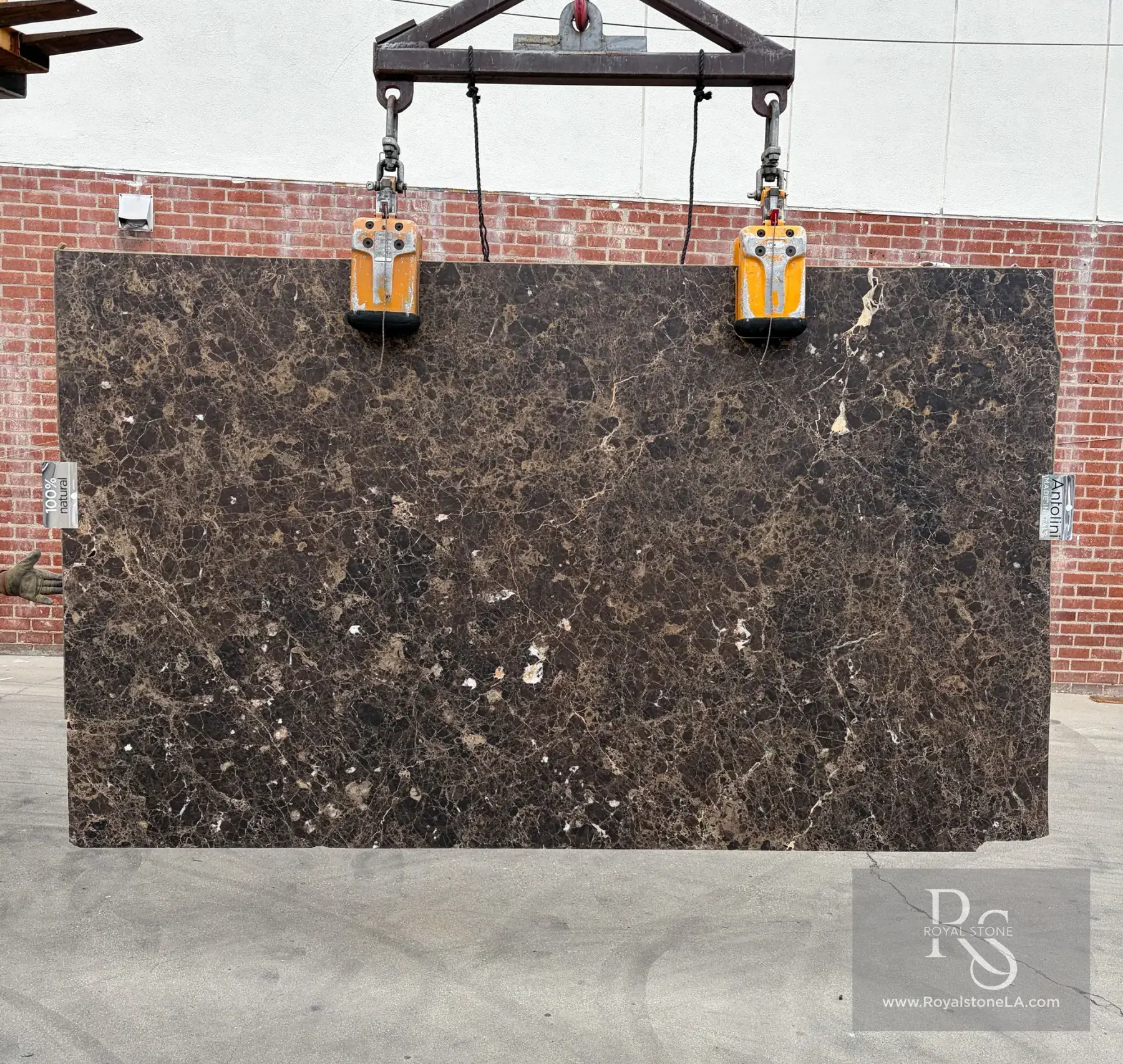 2cm Antolini Emperador Dark YG820 honed marble slab, 70 by 118 inches, deep espresso-brown field with fine caramel and bronze veining and bright white calcite inclusions, lifted by crane against a red brick wall at Royal Stone in Los Angeles