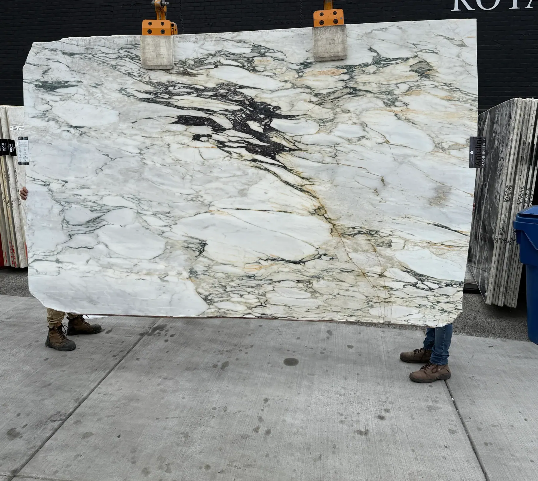 Antolini Monet Viola Classic marble slab YG373 polished at 76 by 119 inches lifted on the crane at Royal Stone Los Angeles, chalk-white field with sage-green and gold veining and a dramatic black ink-splash inclusion