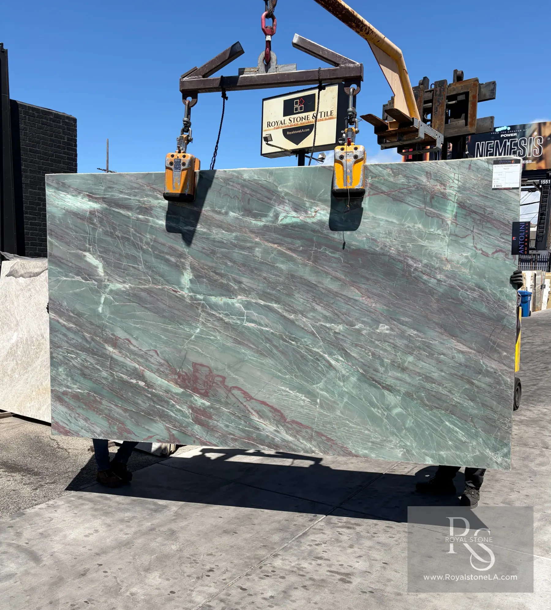 Antolini Thunderflash Quartzite slab in matte finish lifted on the crane against blue sky, soft seafoam-green field crossed by rust-red lightning veining