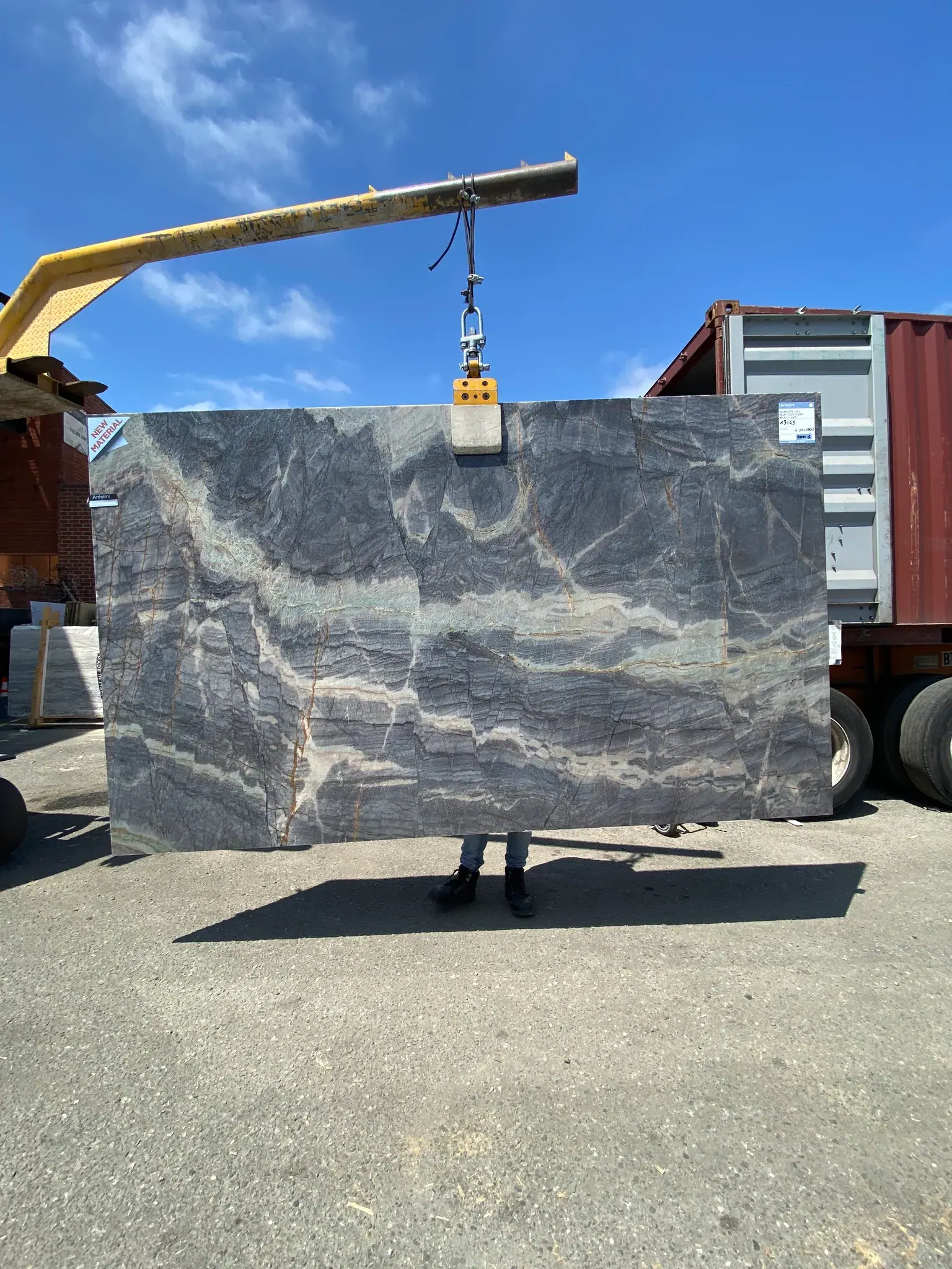 Antolini Blue Deep Liki quartzite slab on the crane at Royal Stone, deep storm grey-blue field with layered horizontal banding and faint gold trace veining, polished finish, 74 by 125 inches