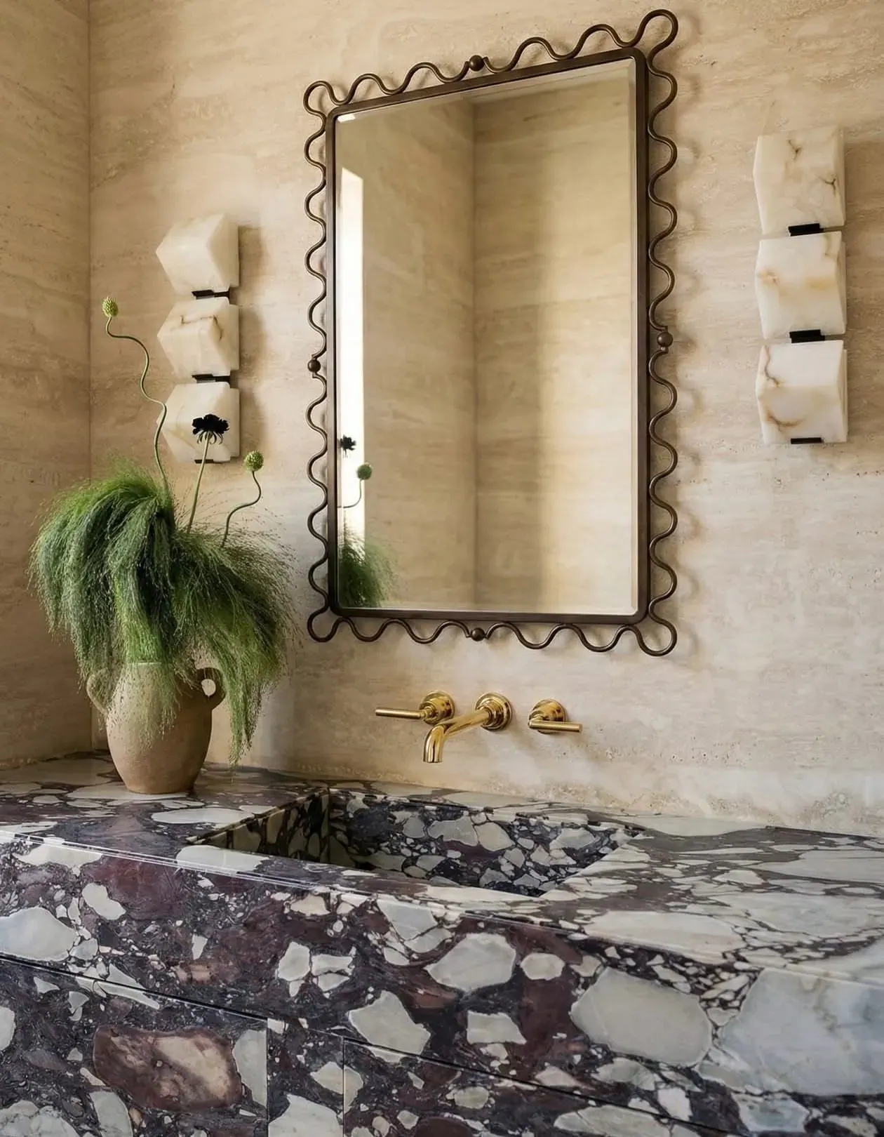 Calacatta Viola Brecciato marble vanity with integrated trough sink, brass wall-mounted fittings, and a travertine surround — burgundy and white brecciated stone read at full scale in a powder bath