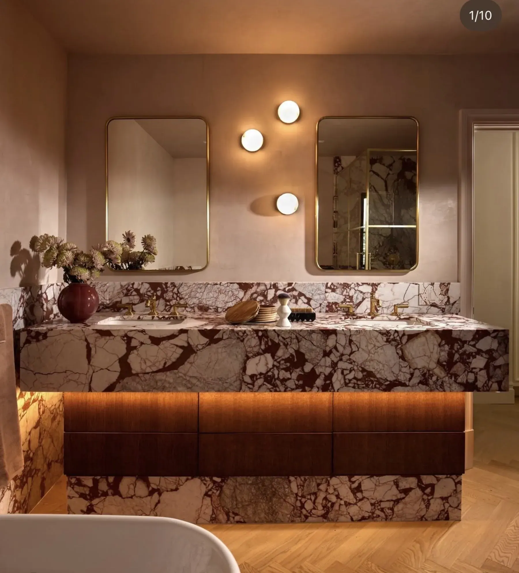 Double vanity wrapped in Calacatta Viola Rosso Extra marble — bookmatched apron and deck against plaster walls, brass fittings, dark wood drawer fronts