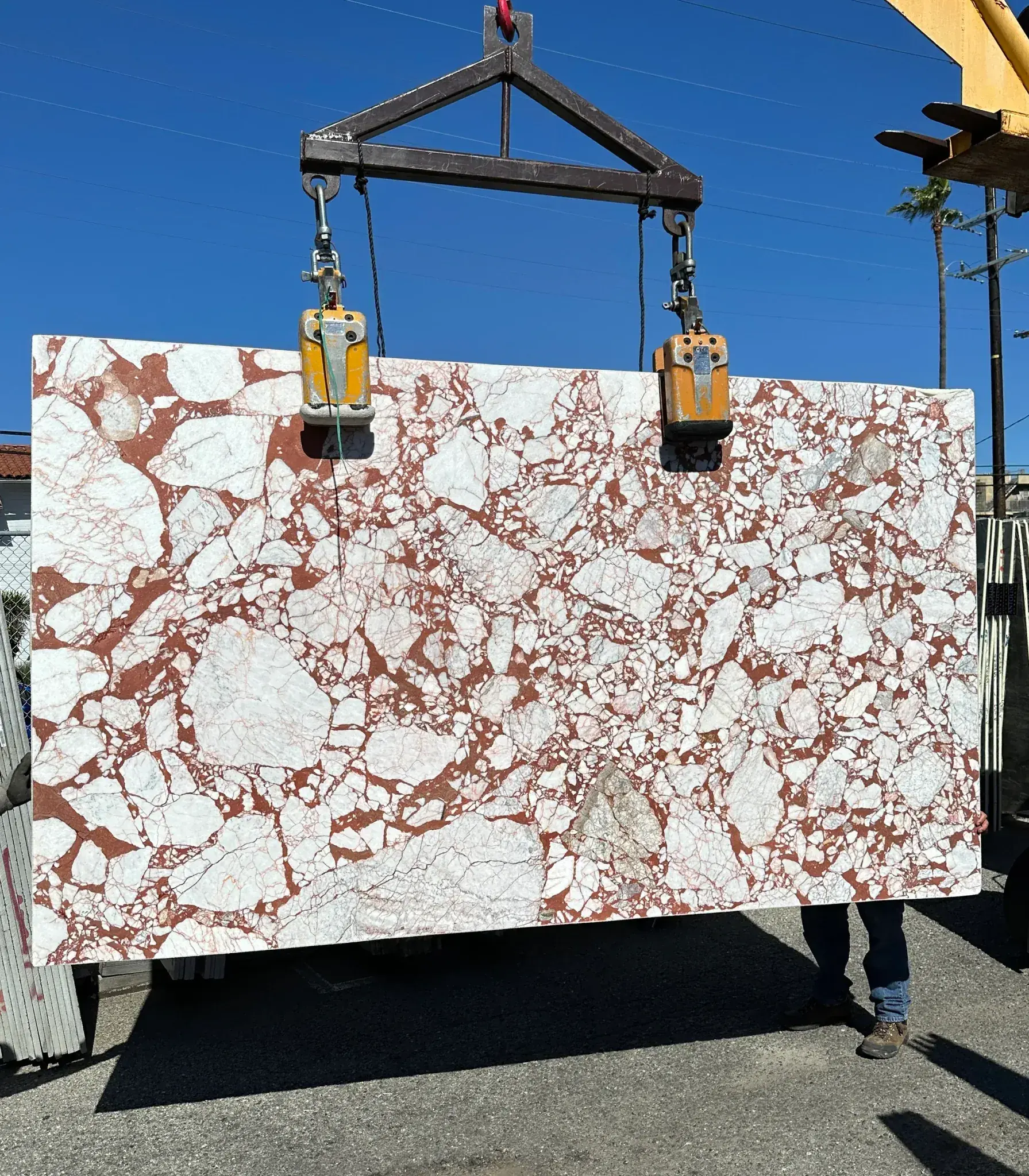 Calacatta Viola Rosso Extra leathered marble slab lifted on crane clamps at Royal Stone — 68 by 116 inches of white Calacatta fragments in a deep red rosso matrix