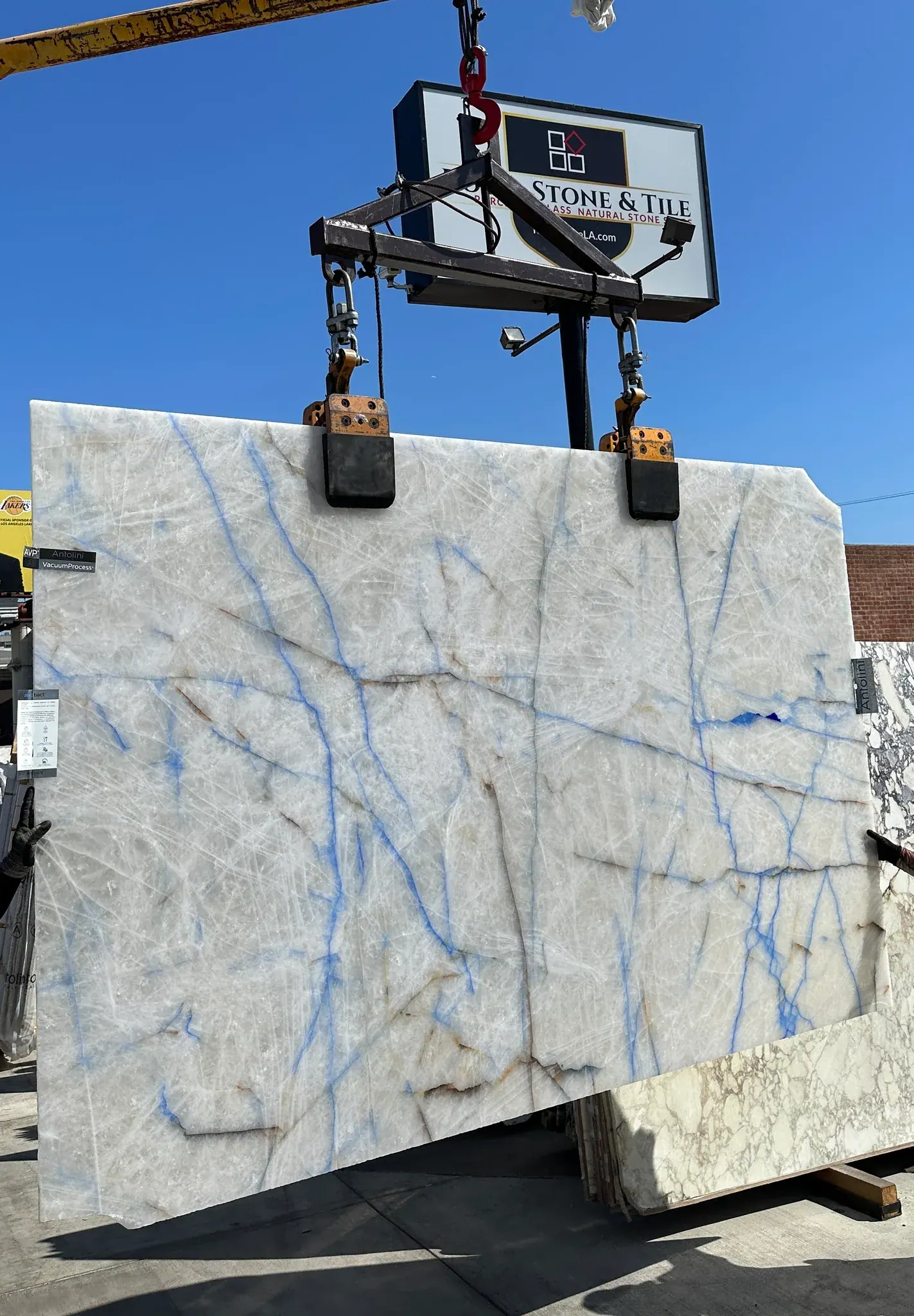 Antolini Cristallo Transazul quartzite slab on the crane, translucent white crystalline quartz field with delicate cobalt-blue veining, polished finish, AVP vacuum process treated, 75 by 116 inches