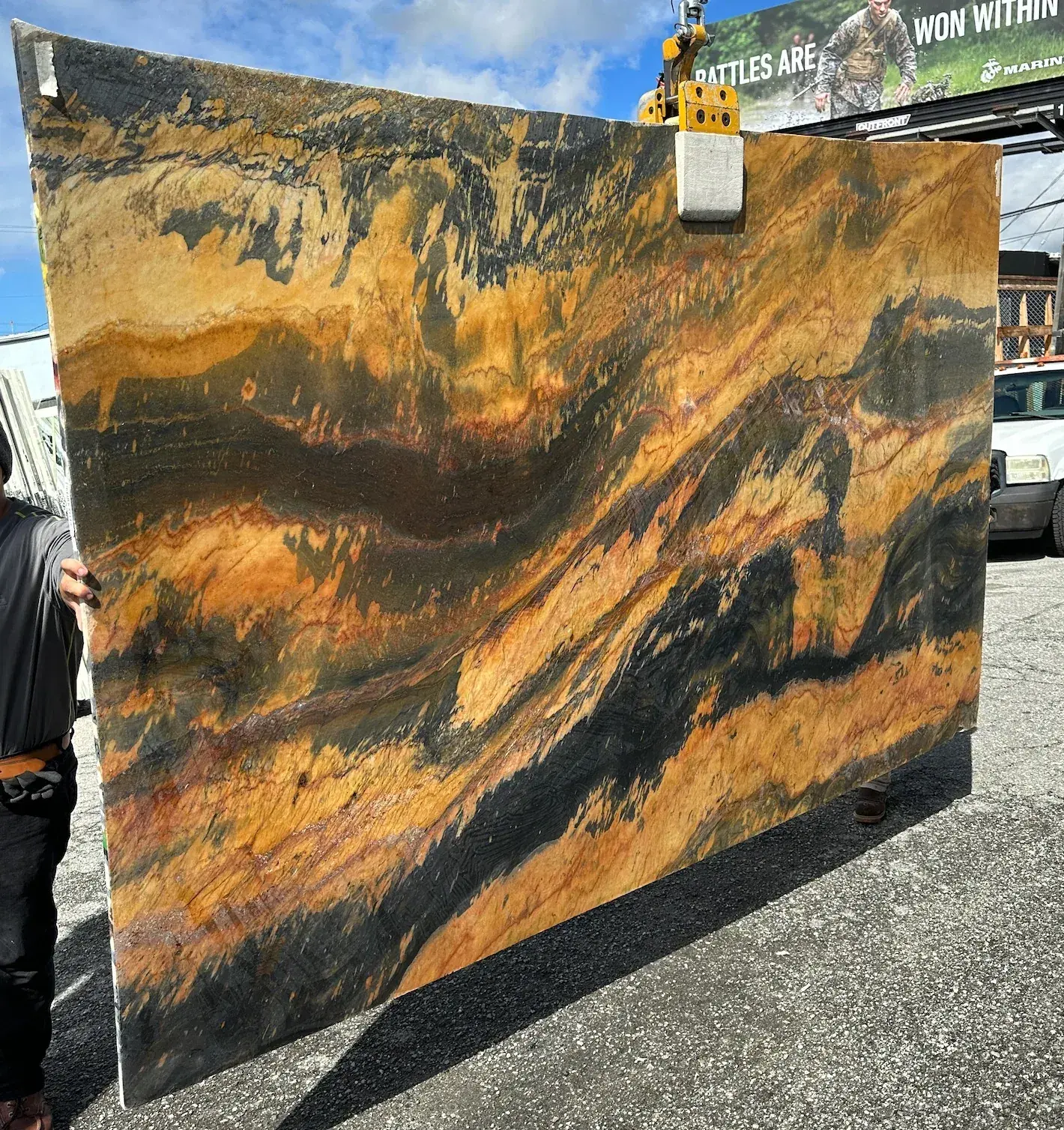 2cm Miami Heat quartzite slab, 117 by 76 inches, polished finish with molten amber and ochre flames driving through deep charcoal banding, lifted by crane in the Royal Stone yard in Los Angeles