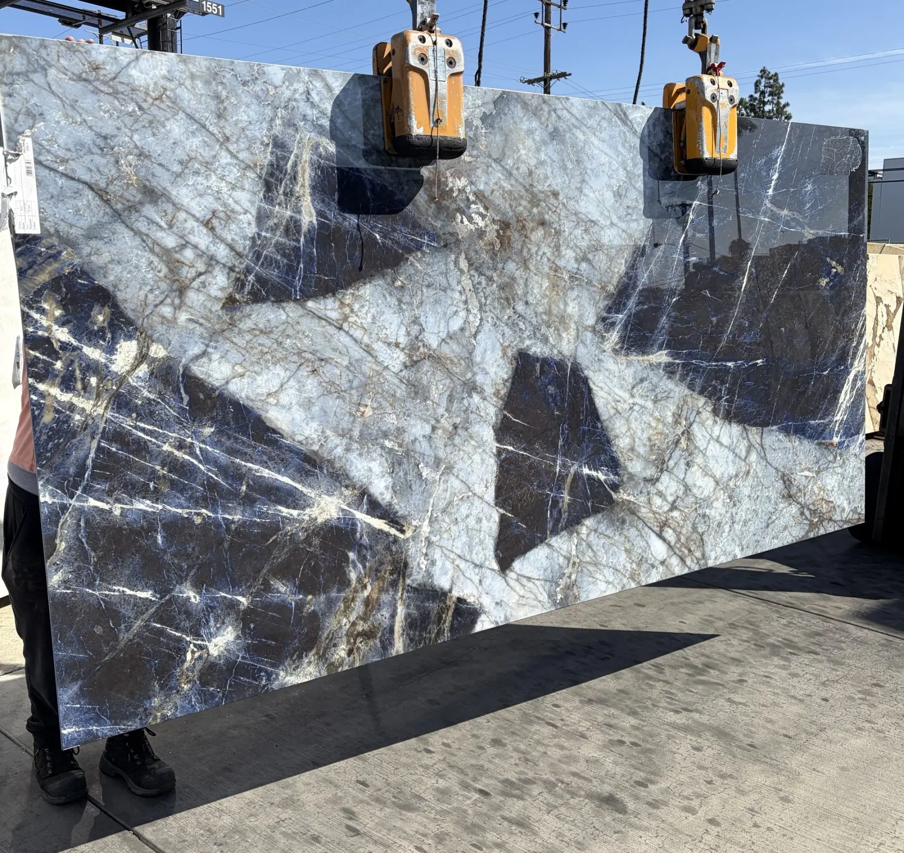 Large-format Patagonia Blue Sodalite Cristallo porcelain panel 1.2cm thickness 63 by 126 inches lifted on a crane in the Royal Stone yard, saturated cobalt and ink-black sodalite fields with icy pale blue translucent passages and copper-rust veining, freshly imported from Italy