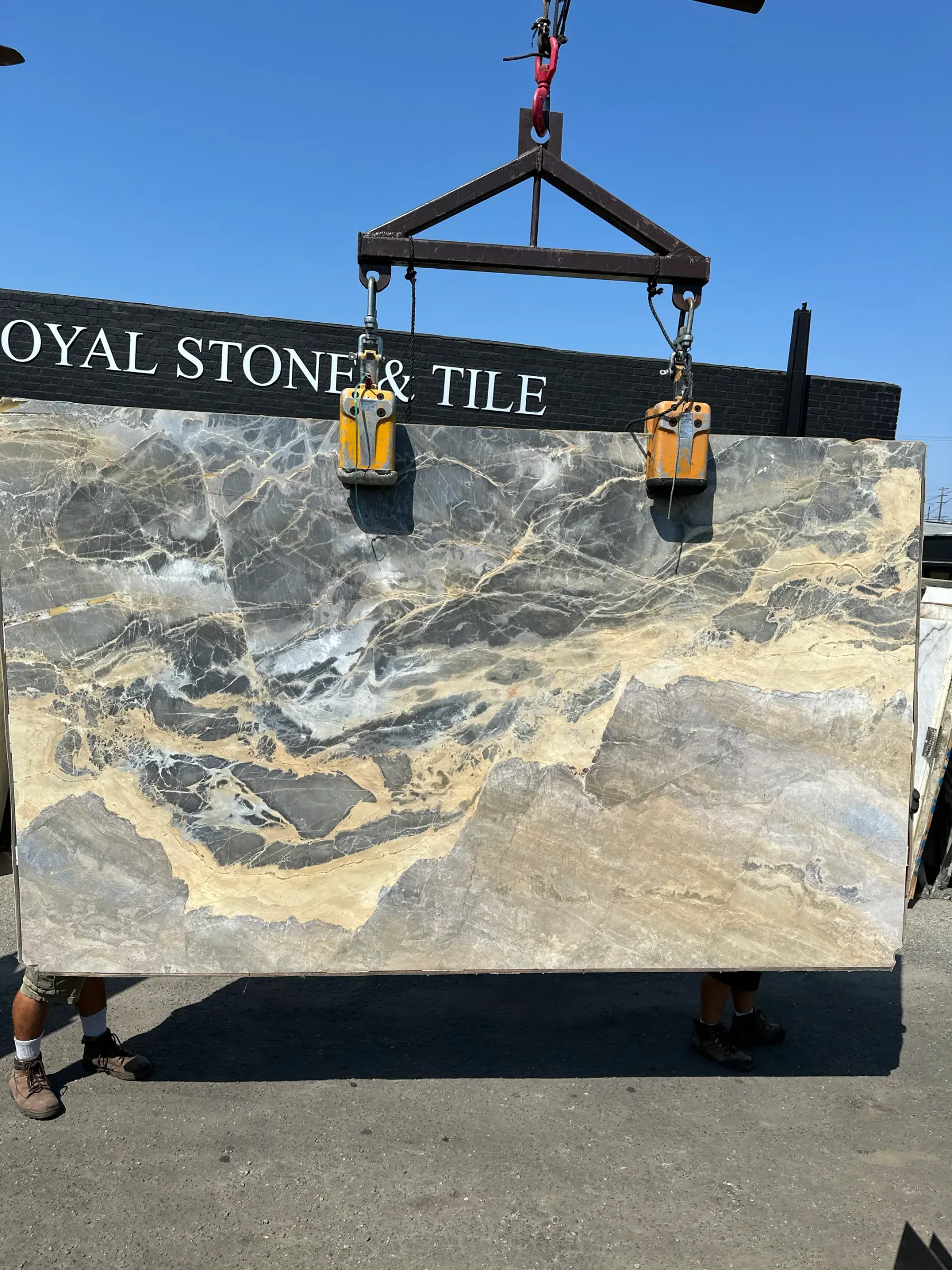 Portoro Gold Tempest marble slab, 78 by 126 inches, polished finish with stormy slate-gray field, molten gold and ochre drift, and fine white quartz veining, lifted by crane in front of the Royal Stone sign in Los Angeles