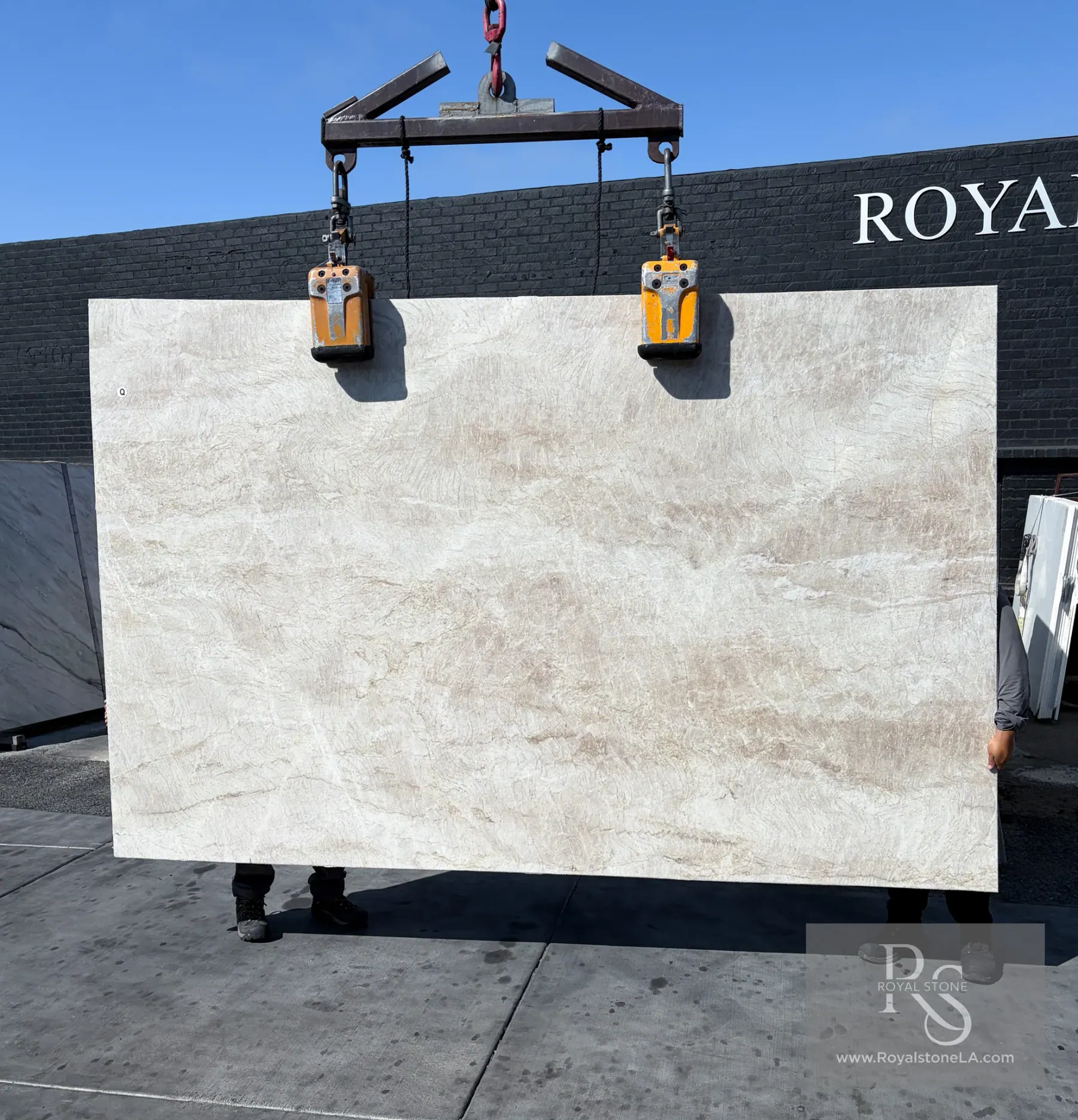 Taj Mahal Select honed quartzite slab lifted on the crane in front of the Royal Stone black brick wall, soft ivory field with low taupe drift