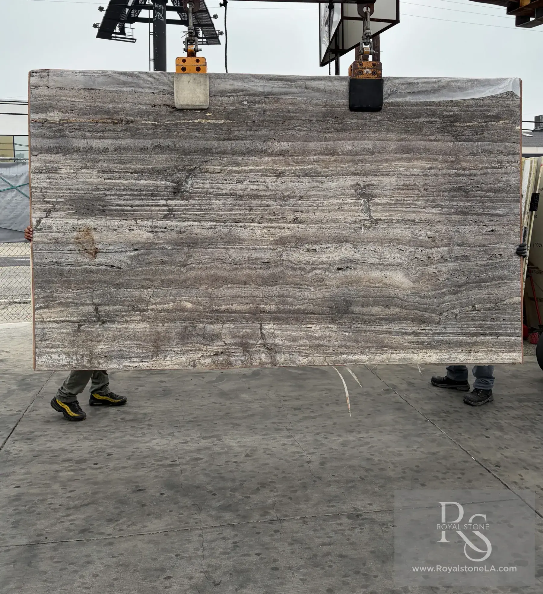 2cm Travertino Titanium charcoal honed and unfilled travertine slab at Royal Stone Los Angeles, cool silver-grey and pewter horizontal stratification with sharper black seams, iron-rust passages, and open vug structure, 73 by 122 inches
