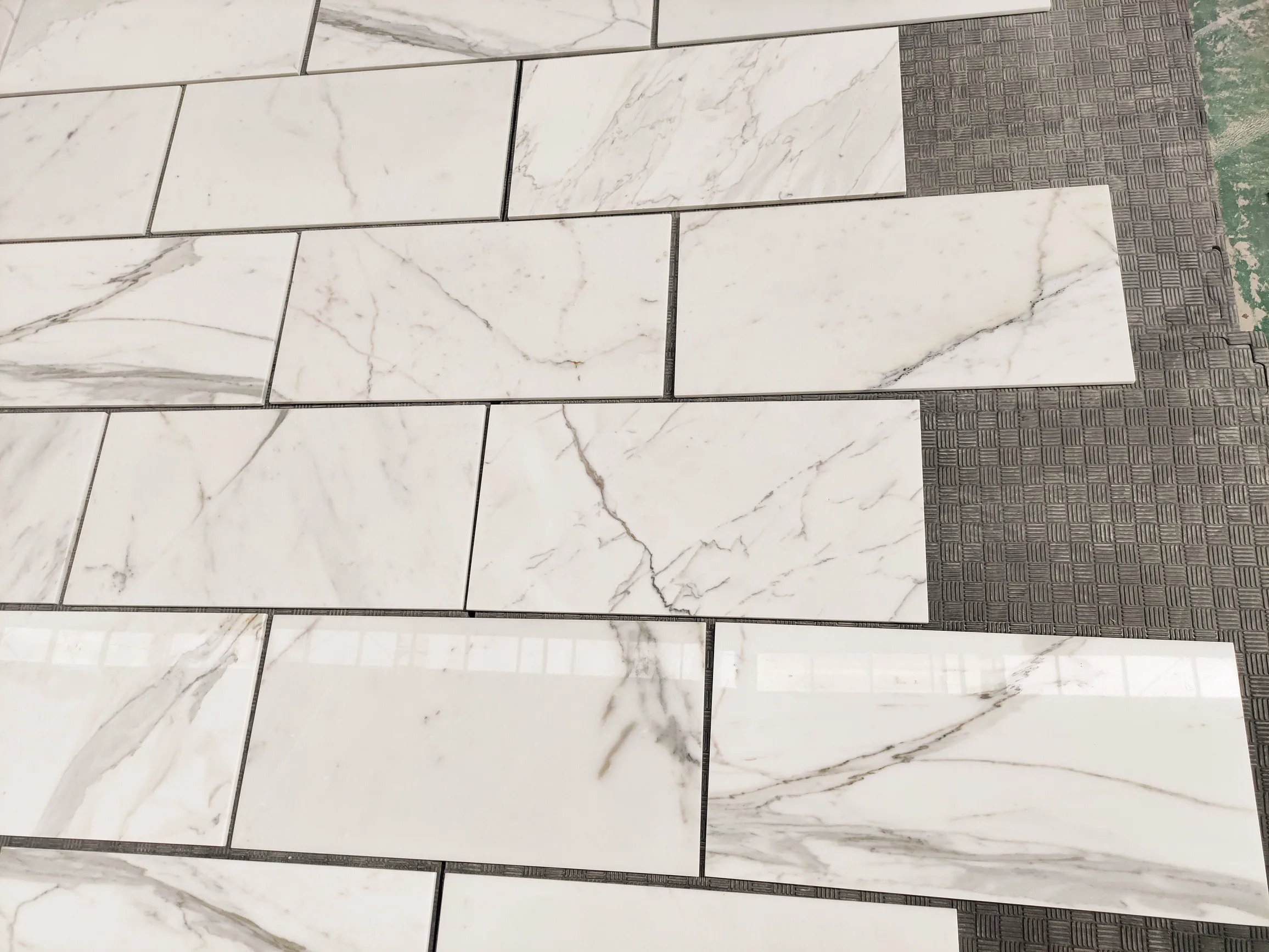 Italian Calacatta Gold 12 by 24-inch marble tile samples being laid out for client approval, paired with a darker Cambrian Black mesh-mounted mosaic strip
