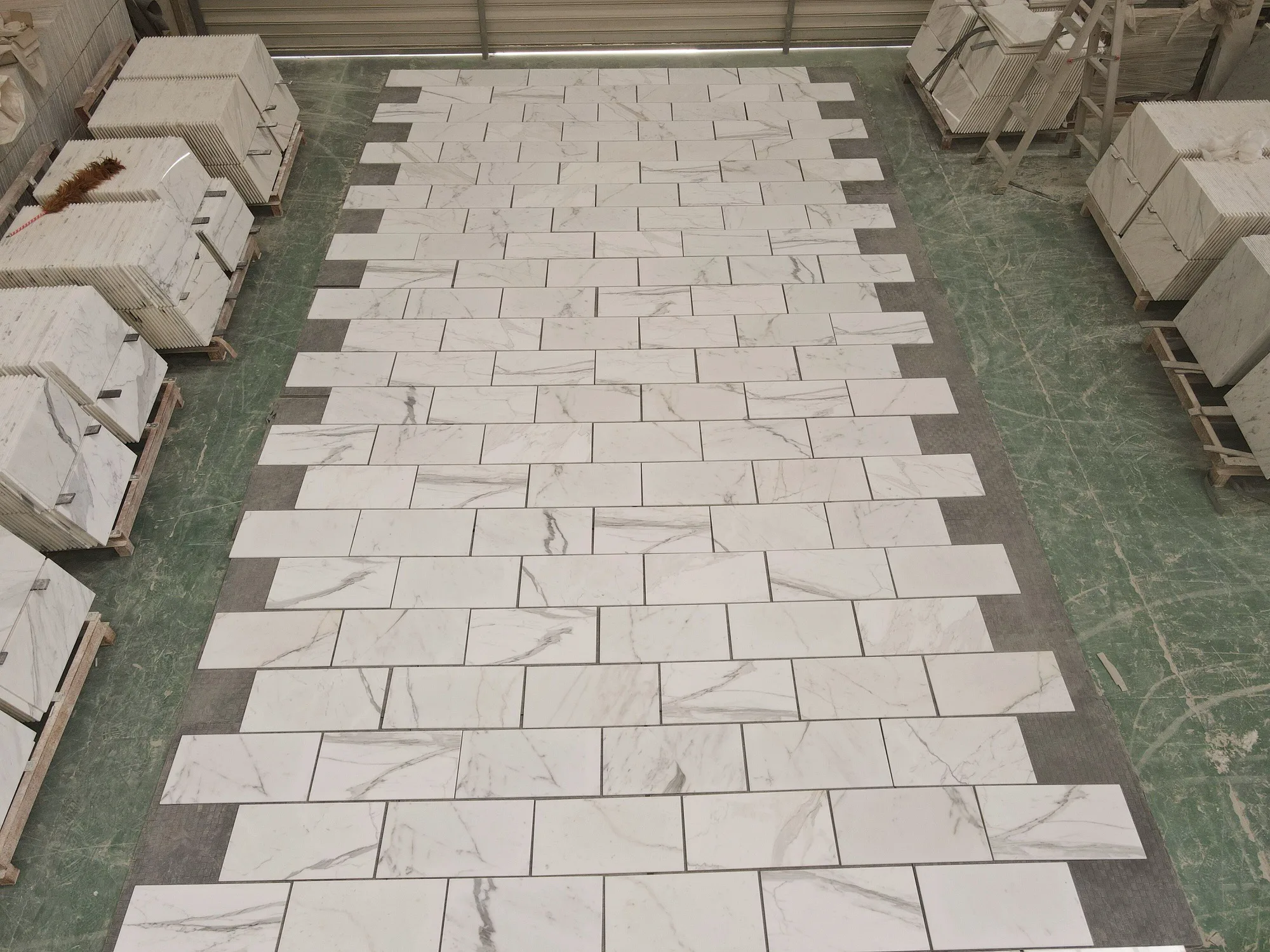 Italian Calacatta Gold 12 by 24-inch marble tile samples being reviewed against a charcoal Cambrian Black border on the Royal Stone approval dock