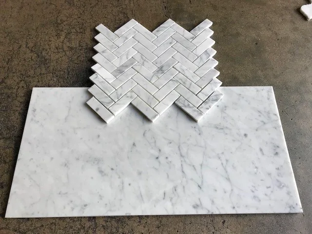 Honed Italian Carrara White marble herringbone mosaic sample above a longer honed field tile, on concrete