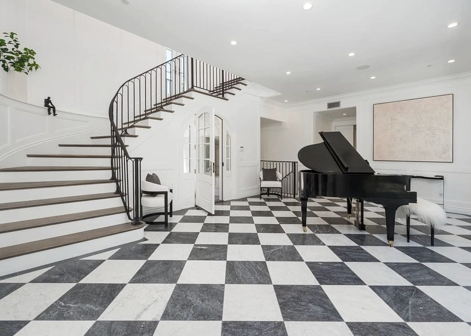 Honed marble checkerboard tile installed in a Los Angeles residence entrance hall, alternating Italian Carrara White and a darker grey marble in 12 by 12-inch squares, paired with a grand piano and a custom spiral staircase
