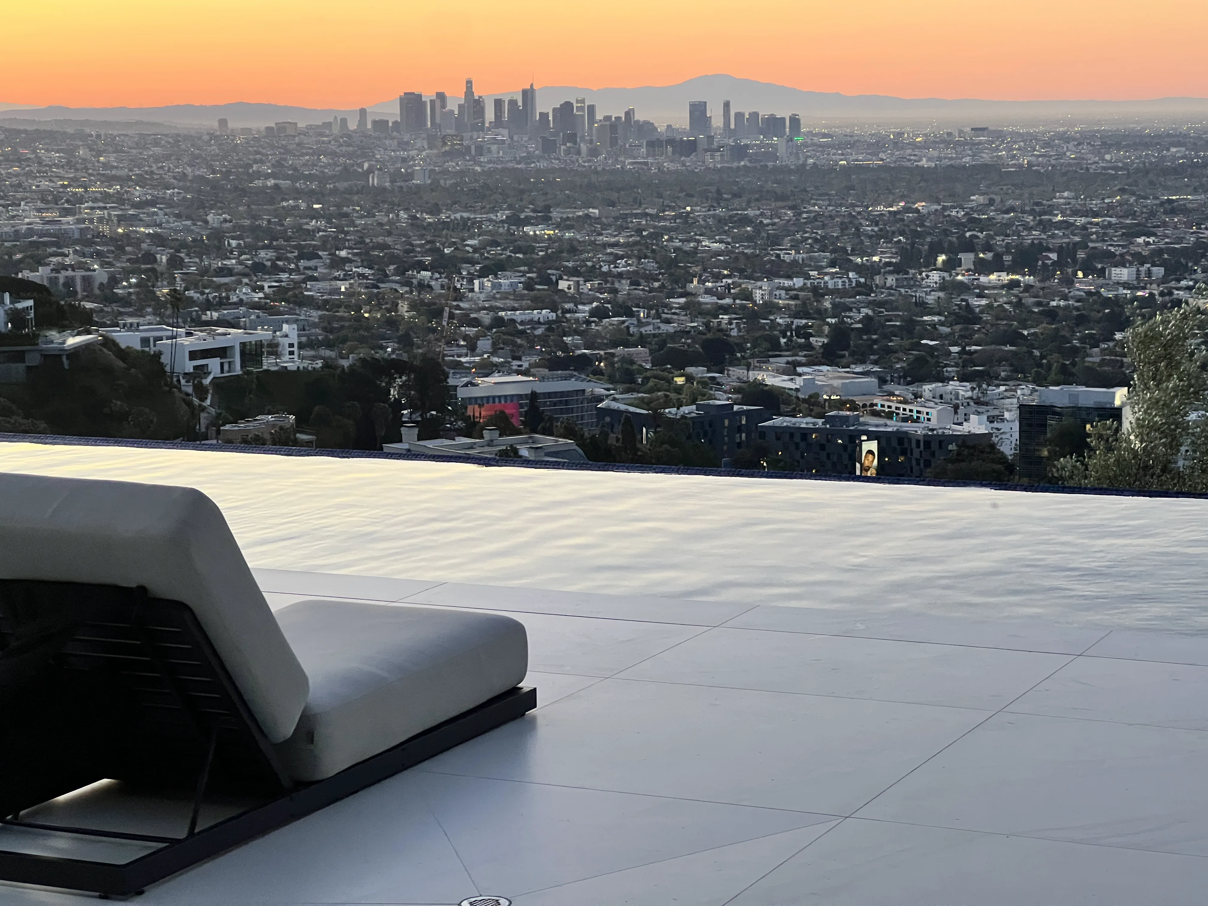 Large-format porcelain tiles laid as an oversized-format patio deck at dusk, with a low chaise overlooking the downtown Los Angeles skyline