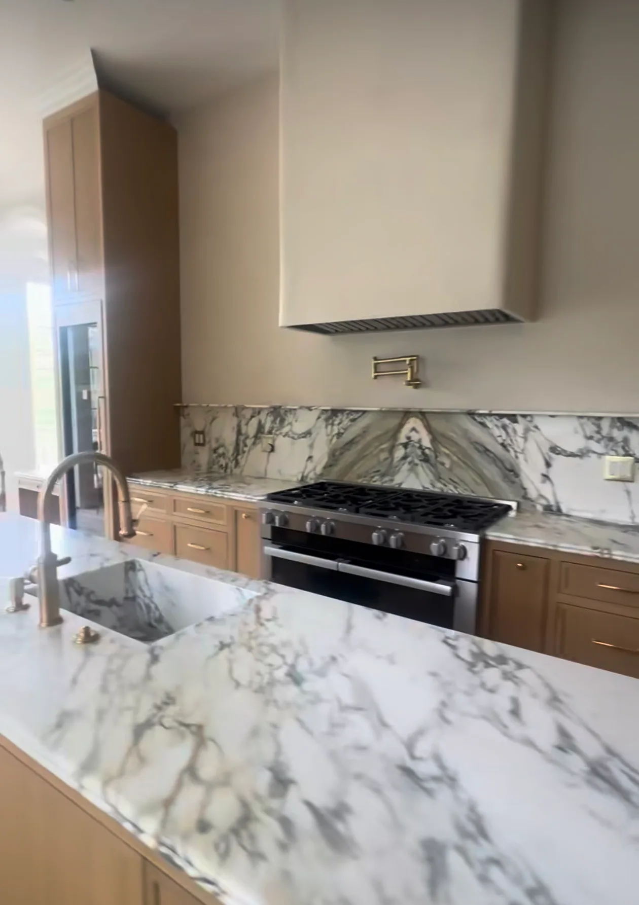 Kitchen with bookmatched Calacatta marble backsplash behind range and Calacatta island countertop with apron sink.